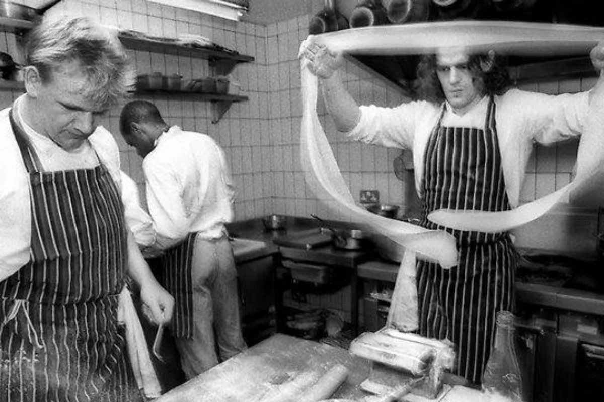 Al interior de una cocina, uno de los cocinero extiende la masa para pasta